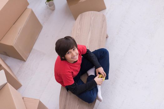 happy little boy sitting on the table with cardboard boxes around him in a new modern home,top view