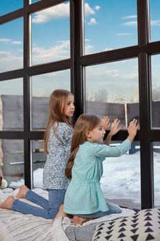 Two beautiful caucasian sisters sitting on the windowsill, they saw something interesting at the window and try to see it