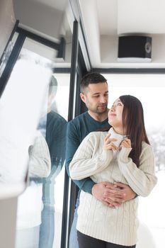 happy young multiethnic couple enjoying morning coffee by the window on cold winter day at home