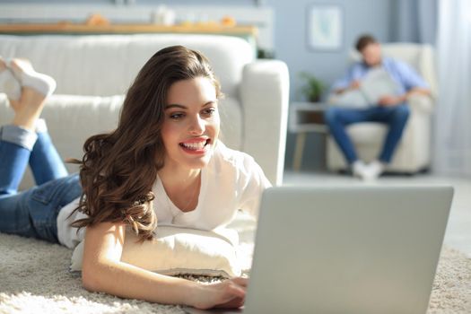 Smiling beautiful woman using laptop with blurred man in background at home