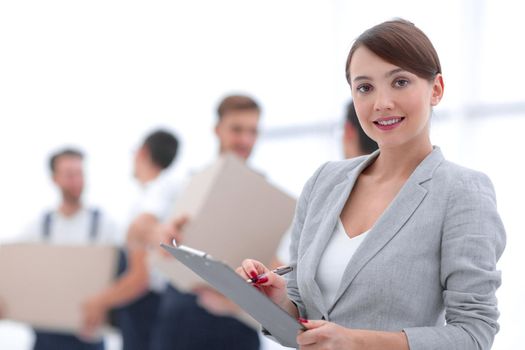 Woman manager holding clipboard on blurred background with movers and boxes.