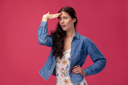 Portrait of a good-looking female in a white dress with floral print and blue denim shirt standing on a pink wall background in studio. She act like she forgot something. People sincere emotions, lifestyle concept. Mockup copy space.