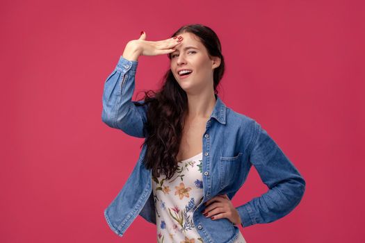 Portrait of a cheerful female in a white dress with floral print and blue denim shirt standing on a pink wall background in studio. She act like she forgot something. People sincere emotions, lifestyle concept. Mockup copy space.