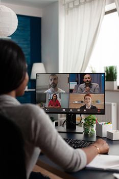 Young adult talking to colleagues on online conference, doing remote work for business project. Employee doing teamwork meeting on video call, using computer and working from home.