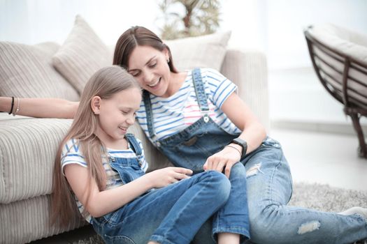 Mother with a little daughter using a smartphone sitting in the new living room.people and technology