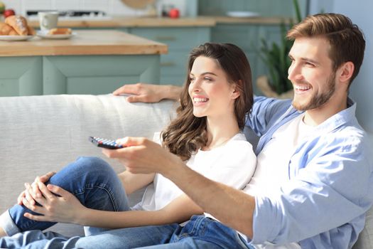 Young loving couple on sofa at home watching tv and laughing