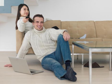 Young multiethnic couple on the sofa watching television together at luxury home