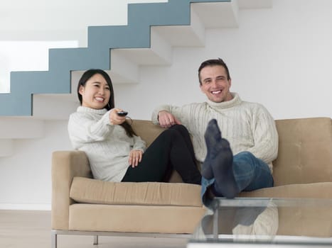 Young multiethnic couple on the sofa watching television together at luxury home