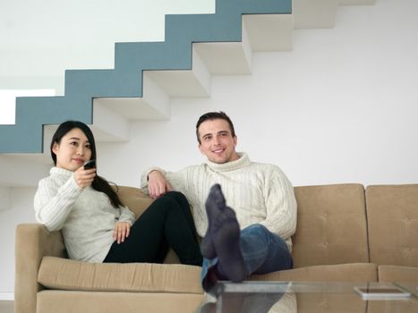 Young multiethnic couple on the sofa watching television together at luxury home