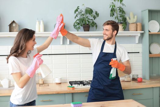 Cheerful young couple giving high five to each other after cleaning flat together