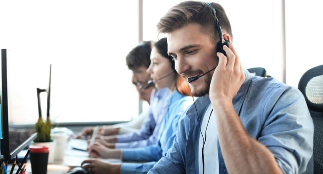 Portrait of call center worker accompanied by his team. Smiling customer support operator at work