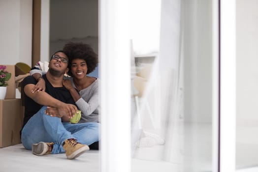 Relaxing in new house. Cheerful young African American couple sitting on the floor and drinking coffee while cardboard boxes laying all around them