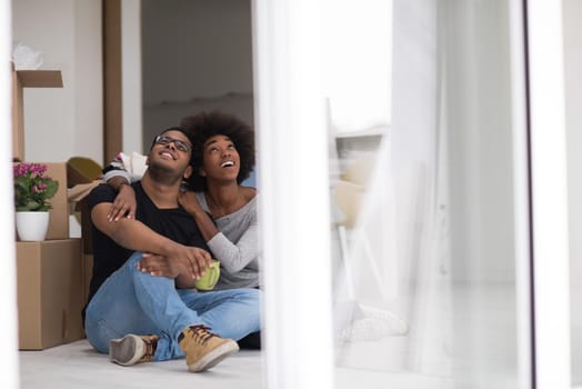 Relaxing in new house. Cheerful young African American couple sitting on the floor and drinking coffee while cardboard boxes laying all around them