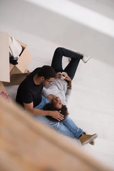 Relaxing in new house. Cheerful young African American couple sitting on the floor and drinking coffee while cardboard boxes laying all around them