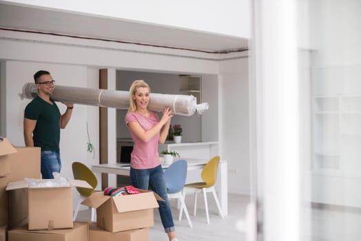 Young couple carrying a carpet moving in to new home together. Home, people, moving and real estate concept