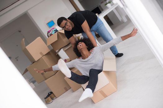 African American couple sitting in a box playing with packing material, having fun after moving in new home