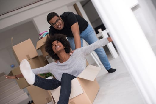 African American couple sitting in a box playing with packing material, having fun after moving in new home