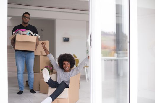 African American couple sitting in a box playing with packing material, having fun after moving in new home