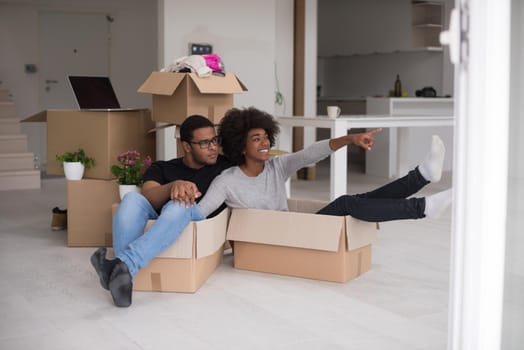 African American couple sitting in a box playing with packing material, having fun after moving in new home