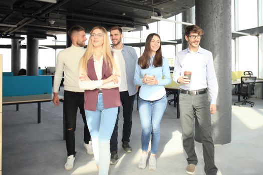 Full length of young people in smart casual wear discussing business and smiling while walking through the office