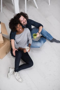 Relaxing in new house. Cheerful young multiethnic couple sitting on the floor and drinking coffee while cardboard boxes laying all around them