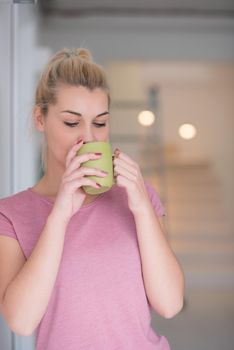 beautiful young woman drinking morning coffee by the window in her home