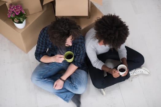 Relaxing in new house. Cheerful young multiethnic couple sitting on the floor and drinking coffee while cardboard boxes laying all around them