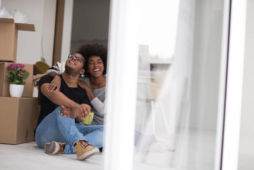 Relaxing in new house. Cheerful young African American couple sitting on the floor and drinking coffee while cardboard boxes laying all around them