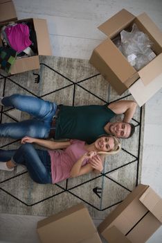 Top view of attractive young couple moving, holding hands, looking at camera and smiling while lying among cardboard boxes