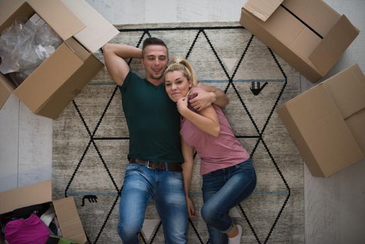 Top view of attractive young couple moving, holding hands, looking at camera and smiling while lying among cardboard boxes