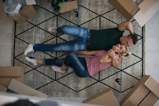 Top view of attractive young couple moving, holding hands, looking at camera and smiling while lying among cardboard boxes