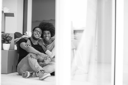 Relaxing in new house. Cheerful young African American couple sitting on the floor and drinking coffee while cardboard boxes laying all around them