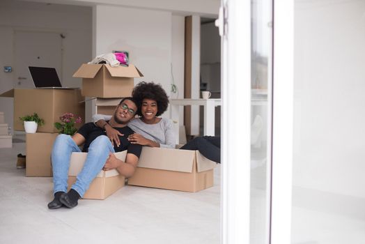 African American couple sitting in a box playing with packing material, having fun after moving in new home