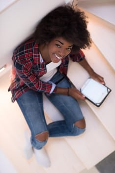 Attractive young black woman using her electronic tablet while sitting on a staircase