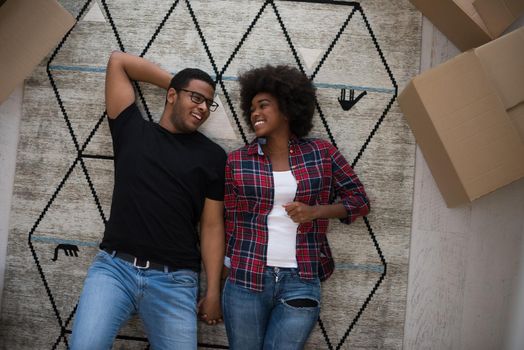 Top view of attractive young African American couple moving, holding hands, looking at camera and smiling while lying among cardboard boxes