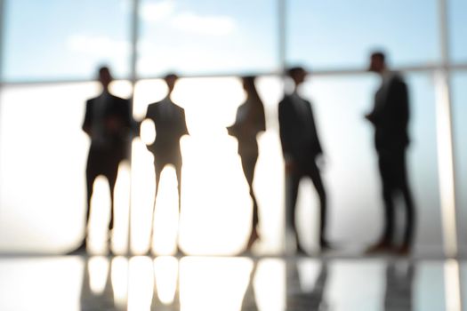 Silhouettes of businesspeople standing against panoramic office window