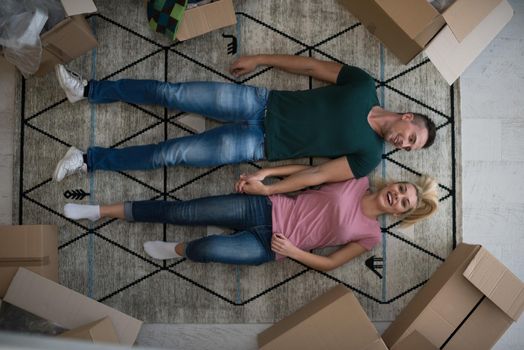 Top view of attractive young couple moving, holding hands, looking at camera and smiling while lying among cardboard boxes