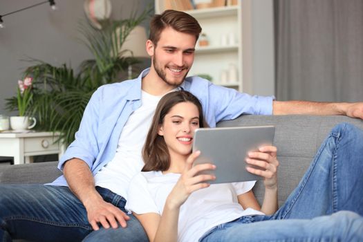 Young couple watching media content online in a tablet sitting on a sofa in the living room