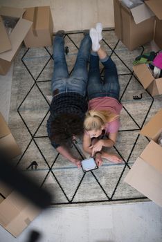 Top view of attractive young couple moving, holding hands, looking at camera and smiling while lying among cardboard boxes