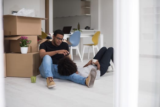 Relaxing in new house. Cheerful young African American couple sitting on the floor and drinking coffee while cardboard boxes laying all around them