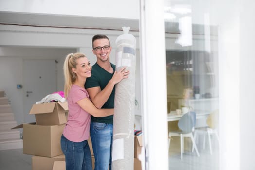 Young couple carrying a carpet moving in to new home together. Home, people, moving and real estate concept