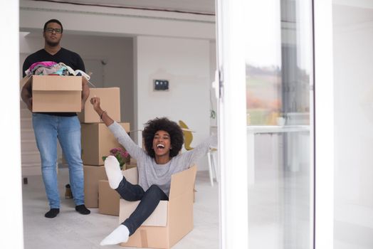 African American couple sitting in a box playing with packing material, having fun after moving in new home