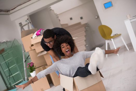 African American couple sitting in a box playing with packing material, having fun after moving in new home