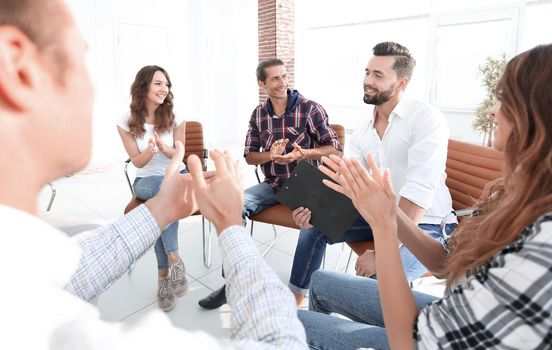 Business people are applauding and smiling while sitting in circle in office