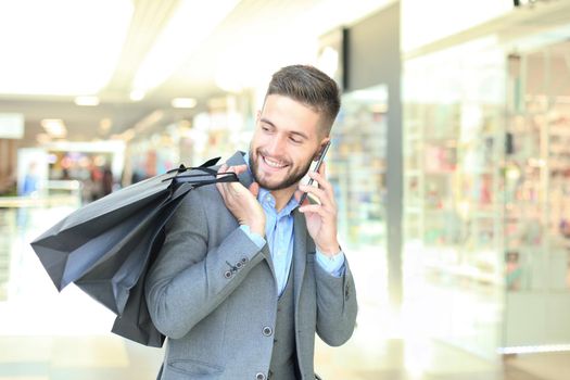 Young businessman with shopping bag talking on the phone indoors