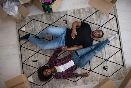 Top view of attractive young African American couple moving, holding hands, looking at camera and smiling while lying among cardboard boxes