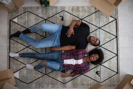 Top view of attractive young African American couple moving, holding hands, looking at camera and smiling while lying among cardboard boxes