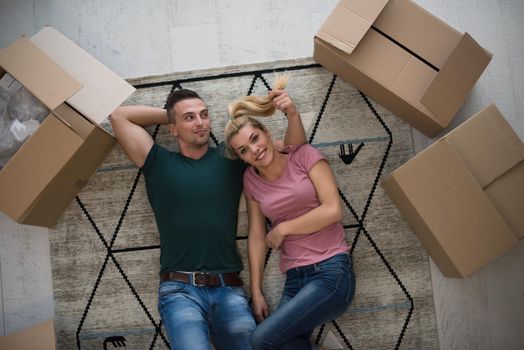 Top view of attractive young couple moving, holding hands, looking at camera and smiling while lying among cardboard boxes