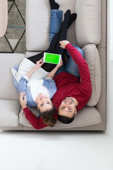 Young couple relaxing at  home using tablet computers reading in the living room on the sofa couch.