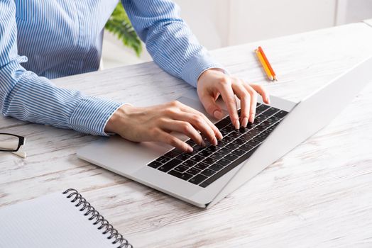 Close up business woman hands typing at laptop keyboard. Side view office workplace with computer on white wooden table. Professional business occupation design with secretary working at desk.